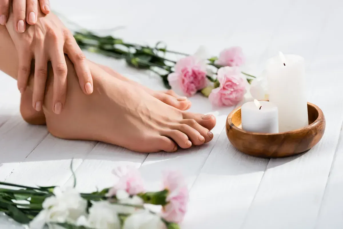 Una mujer toca sus pies junto a un cuenco de velas y flores.