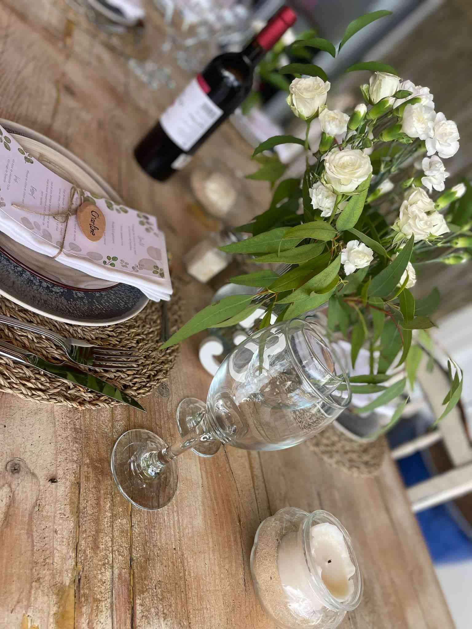 Una mesa de madera con platos, copas de vino, velas y flores sobre ella.