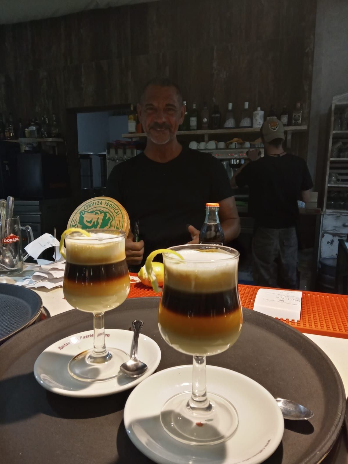 Un hombre está sentado en una mesa con dos bebidas en una bandeja.