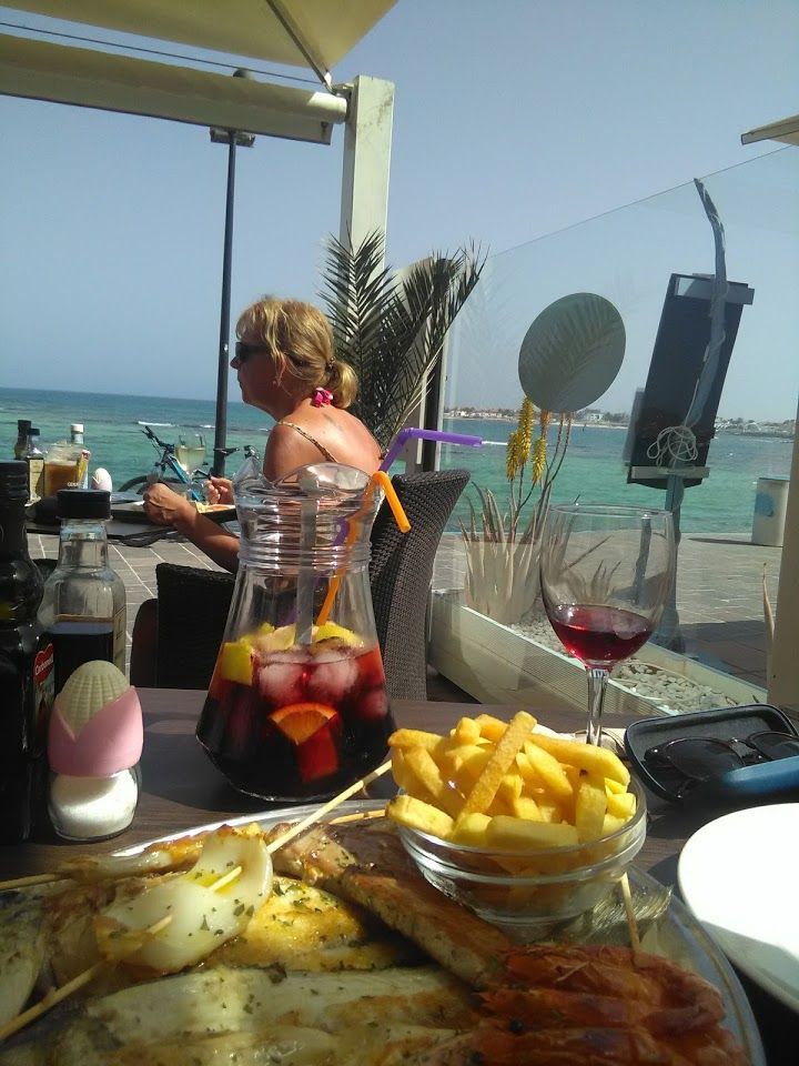 Una mujer se sienta a una mesa con una jarra de sangría y un tazón de papas fritas.