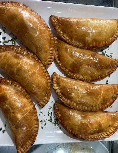 Empanadas doradas horneadas dispuestas en un plato blanco, adornadas con hierbas verdes.