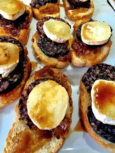 Rebanadas de baguette tostadas cubiertas con morcilla, cebollas caramelizadas y queso de cabra.