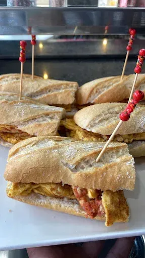 Sándwiches en un plato blanco, sostenidos con la mano. Cada baguette contiene una tortilla gruesa, sujeta con un palillo decorativo.