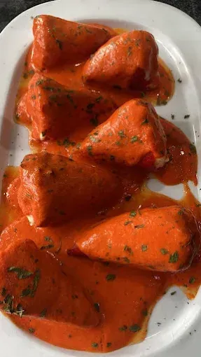 Pimientos rellenos de naranja en una vibrante salsa de tomate, adornados con perejil, en un plato blanco.