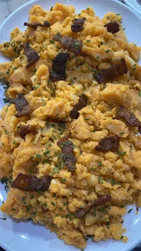 Huevos revueltos con tocino y perejil en un plato blanco.