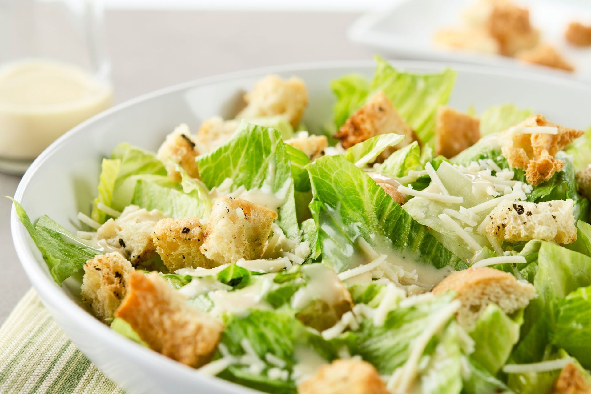 Ensalada César con crutones, queso parmesano y aderezo cremoso en un tazón blanco.