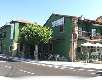 Un edificio verde con mesas y sombrillas delante.