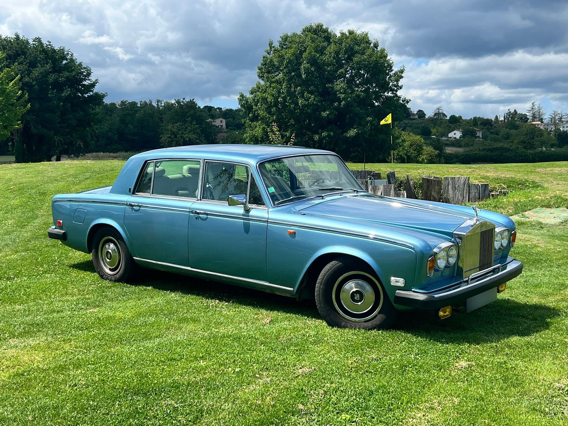 Rolls royce bleue sur herbe et arbres en fond