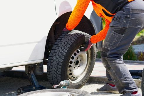 Persona con mangas naranjas cambiando una llanta de una camioneta blanca, usando un gato.