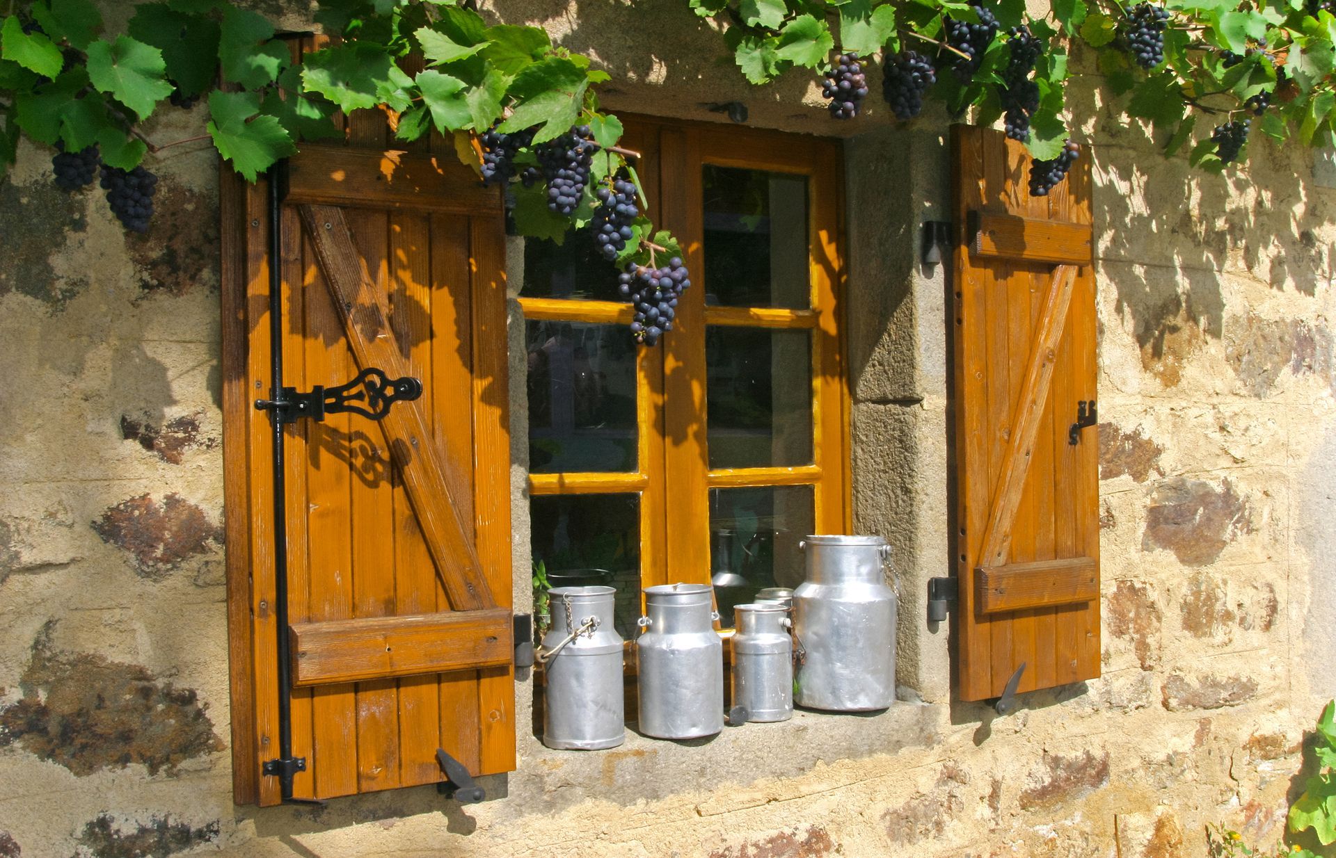 Des volets en bois encadrent une fenêtre avec des bidons de lait sur le rebord.