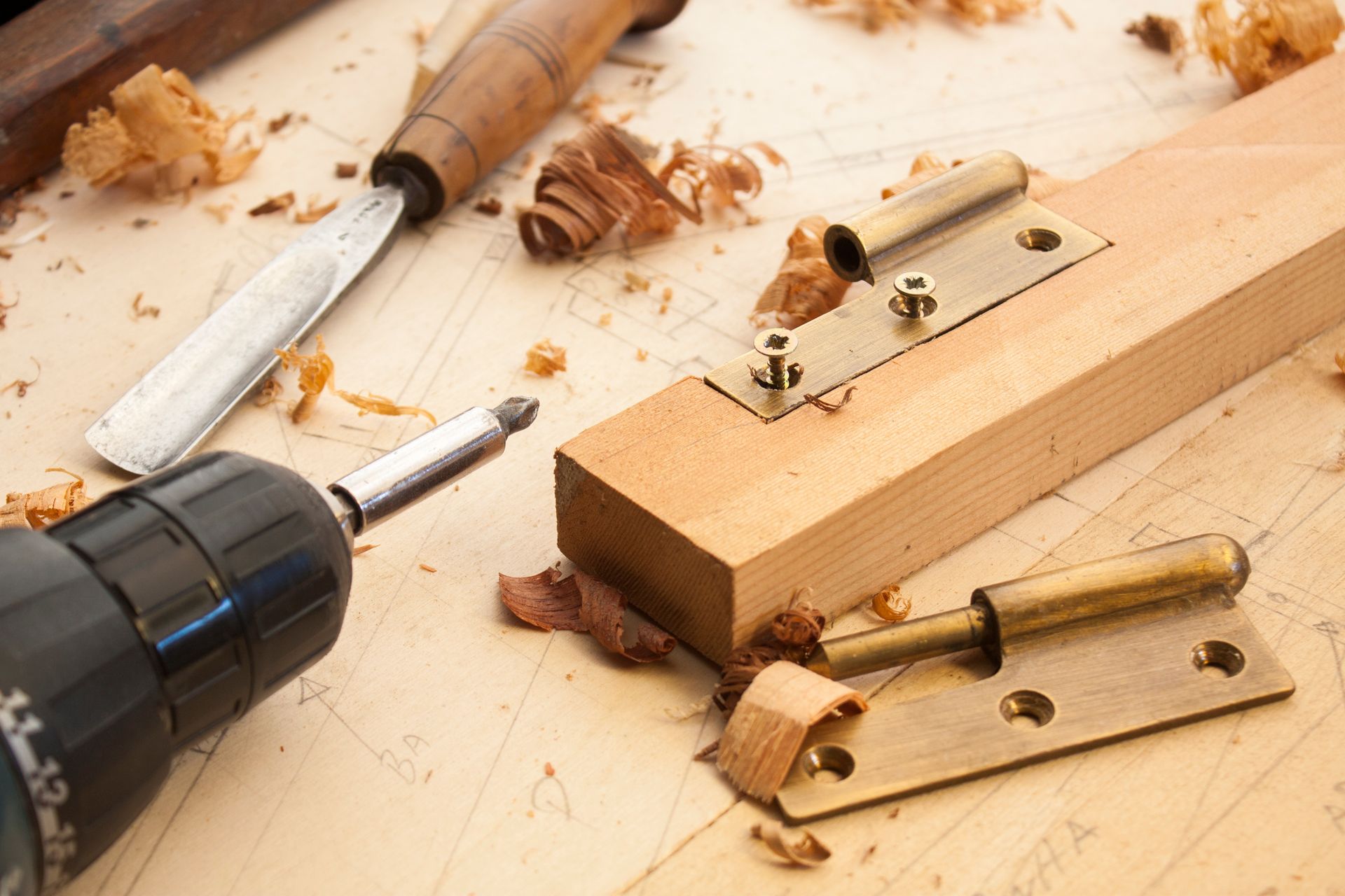 Scène de travail du bois : une perceuse, un ciseau et une charnière en laiton sont installés sur un bloc de bois.