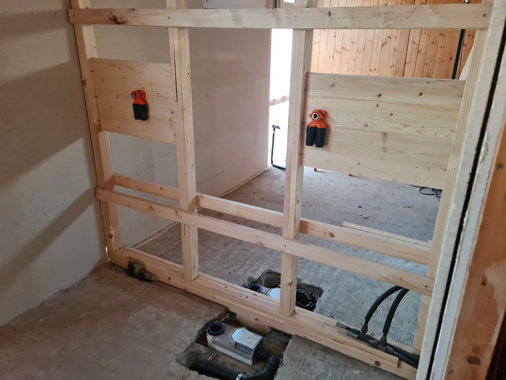 Unfertige Innenwandkonstruktion mit freiliegenden Ständern, Elektroverteilerkästen und Betonboden.