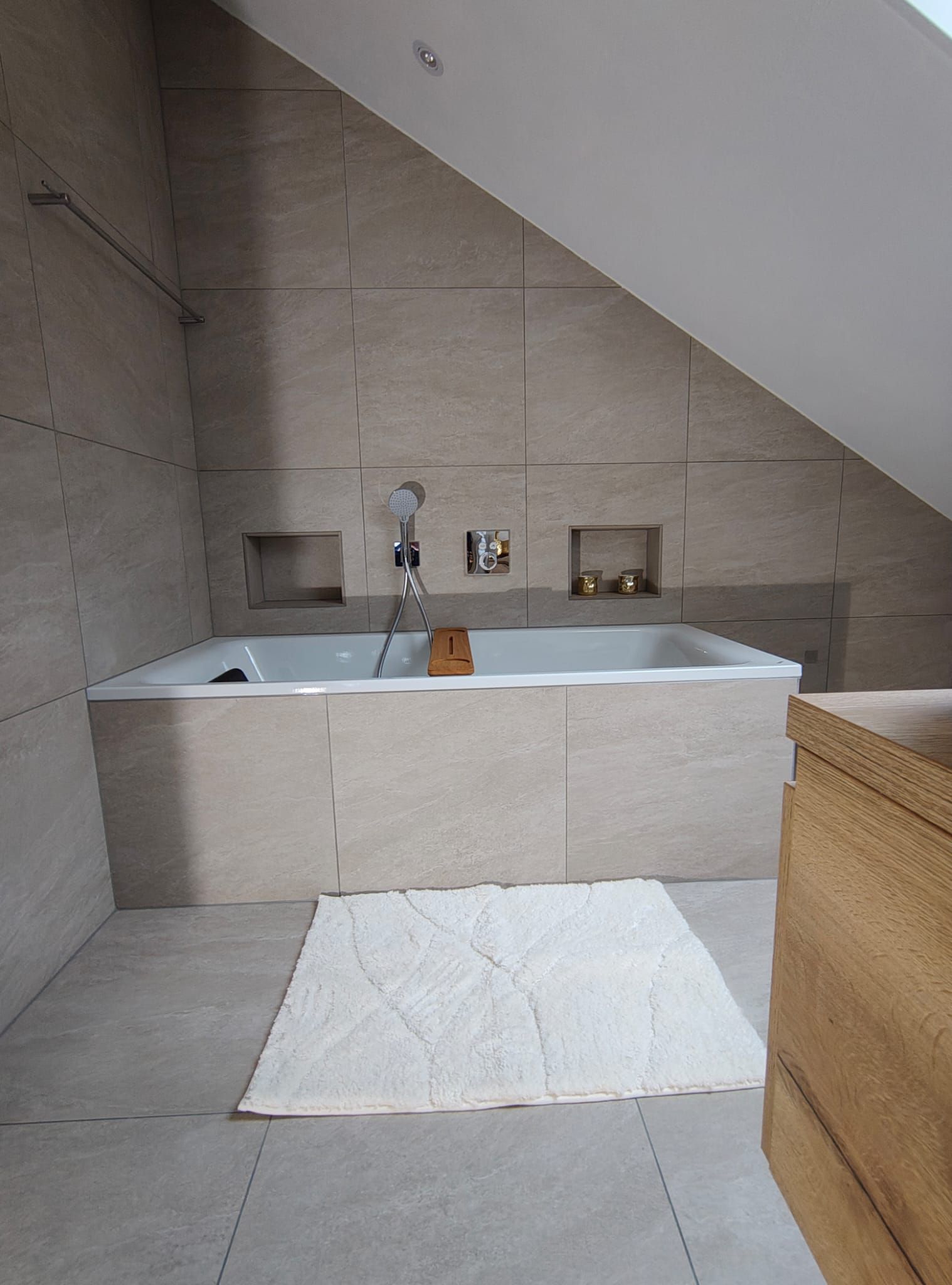 Kleines gefliestes Badezimmer mit rechteckiger Badewanne, weisser Badematte und einem geflochtenen Korb.