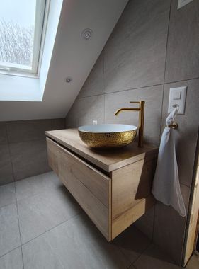 Kleines gefliestes Badezimmer mit rechteckiger Badewanne, weisser Badematte und einem geflochtenen Korb.