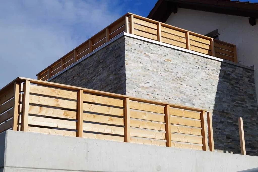 Modernes Steinhaus mit hellen Holzbalkongeländern vor blauem Himmel