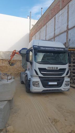 Un camión volquete Iveco está estacionado en un lote de tierra frente a un edificio.