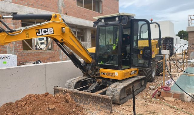 Una excavadora JCB amarilla y negra está estacionada frente a un edificio en construcción.