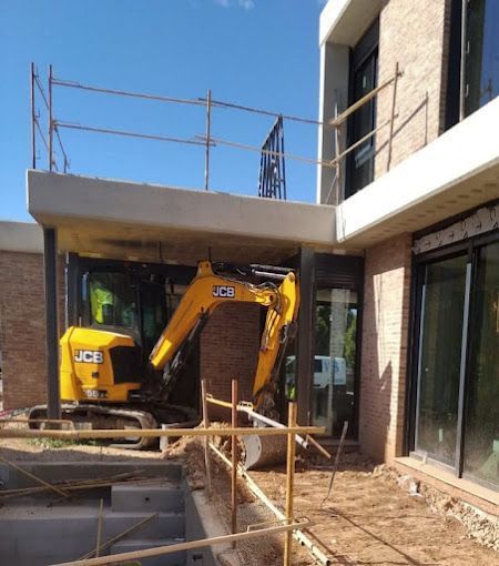Una excavadora JCB amarilla está estacionada frente a un edificio en construcción.