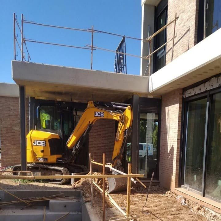 Una excavadora JCB amarilla está estacionada frente a un edificio de ladrillos.