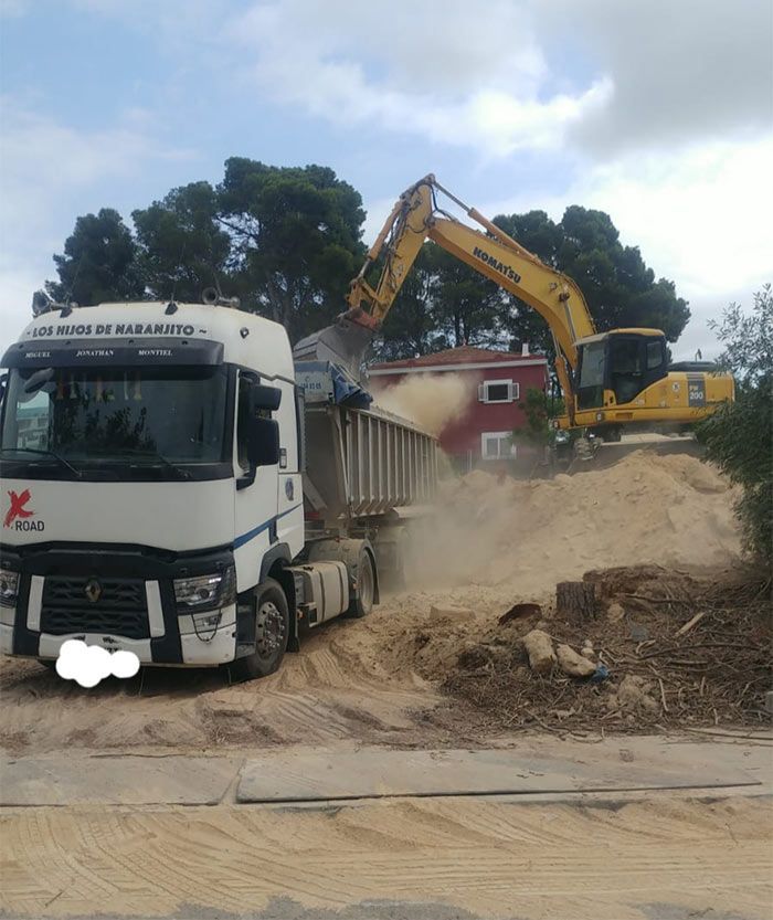 Un camión blanco circula por un camino de tierra al lado de una excavadora amarilla.