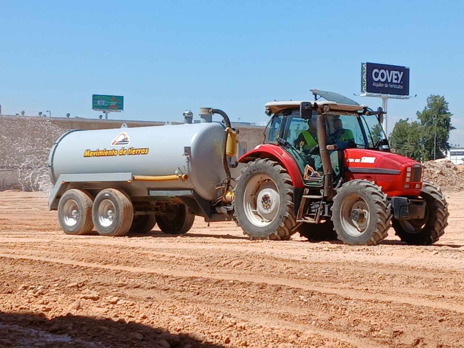 Un hombre empuja una carretilla junto a una excavadora en un camino de tierra.
