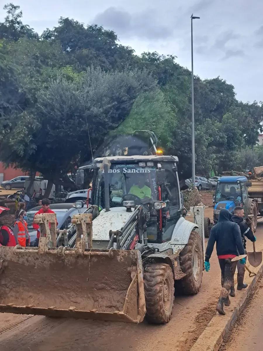 Un hombre empuja una carretilla junto a una excavadora en un camino de tierra.