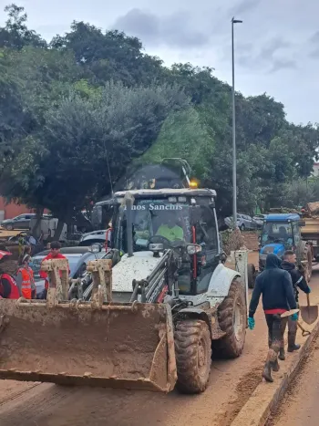 Un hombre empuja una carretilla junto a una excavadora en un camino de tierra.