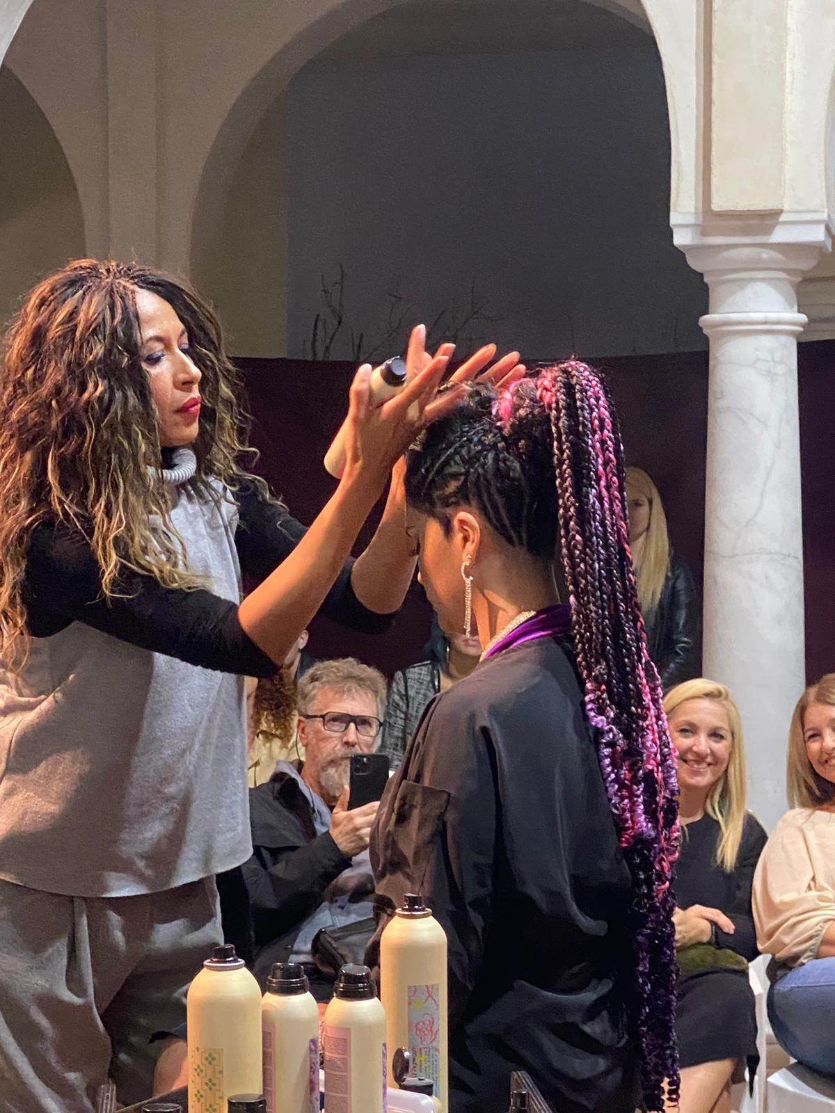 Estilista arregla el cabello trenzado de una modelo en un escenario frente a una audiencia en un salón