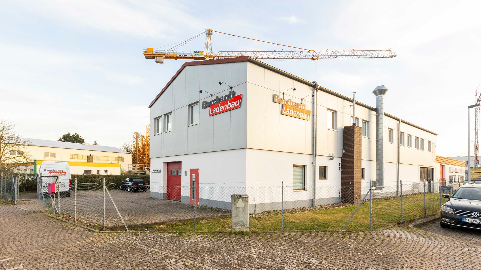 ein großes weißes Gebäude mit einem Kran darauf und einem davor geparkten Auto.