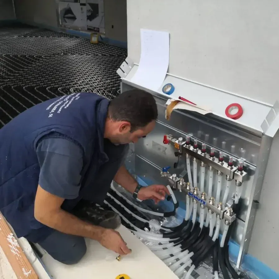 Fontanero instalando tuberías a un colector para calefacción por suelo radiante; entorno interior.