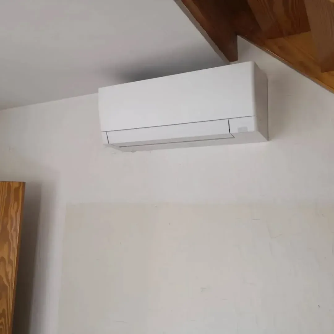 Unidad de aire acondicionado blanca montada en una pared blanca bajo vigas de madera.