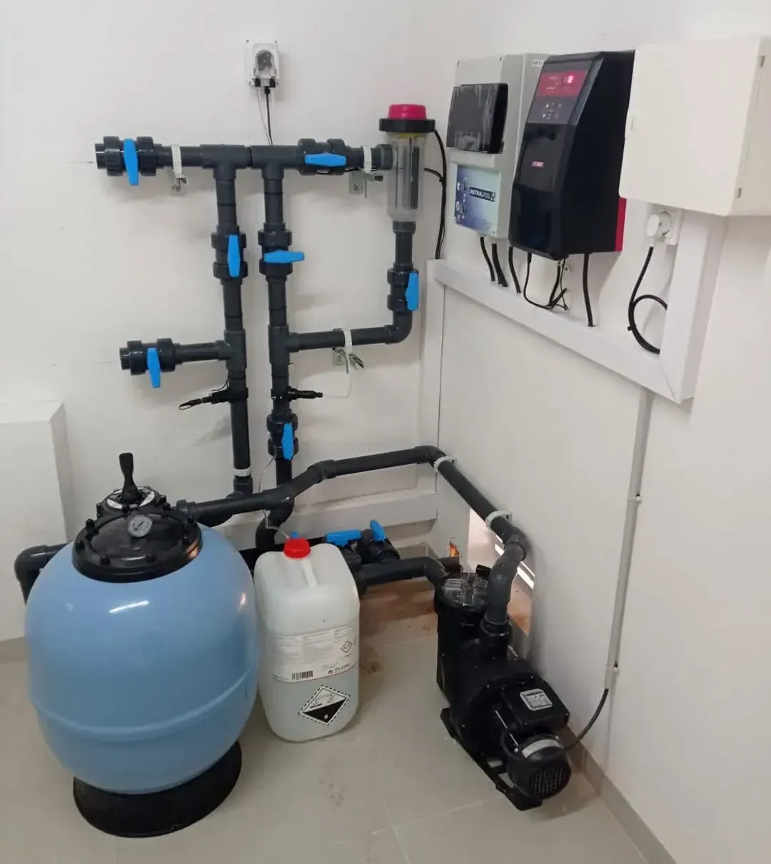 Sistema de filtración de piscina con tuberías, bomba, filtro y panel de control. Colores azul, negro y blanco.