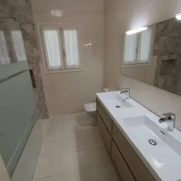 Baño con un tocador largo, dos lavabos e inodoro. Tonos blanco y madera clara.