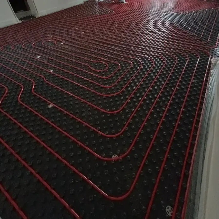 Tubería roja colocada sobre un sistema de calefacción por suelo radiante negro, lista para la instalación del suelo.