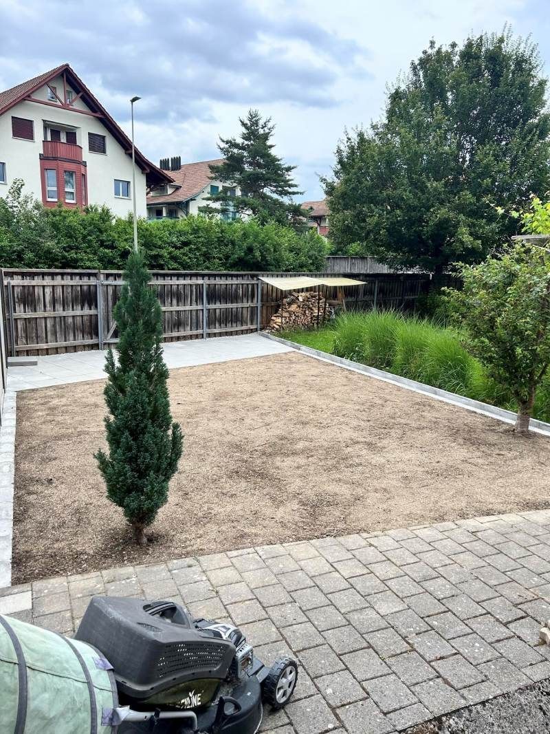 Ein Rasenmäher steht auf einer gemauerten Terrasse in einem Hinterhof. Foto  von Edi Gartenunterhalt.