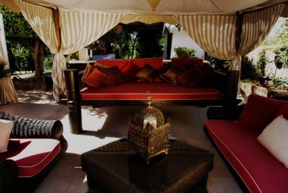 Zona de estar al aire libre con cojines rojos, linterna adornada y dosel drapeado.