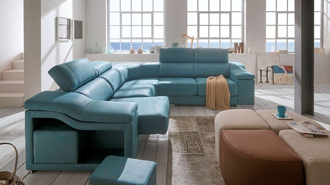 Una sala de estar con un sofá seccional azul y dos otomanas.