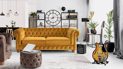 Una sala de estar con un sofá amarillo, una silla, una otomana, una guitarra y un reloj.