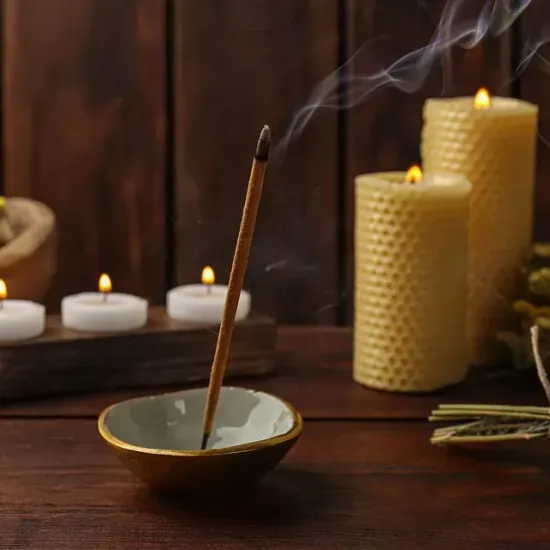 Un cuenco de varillas de incienso está sobre una mesa de madera al lado de velas.