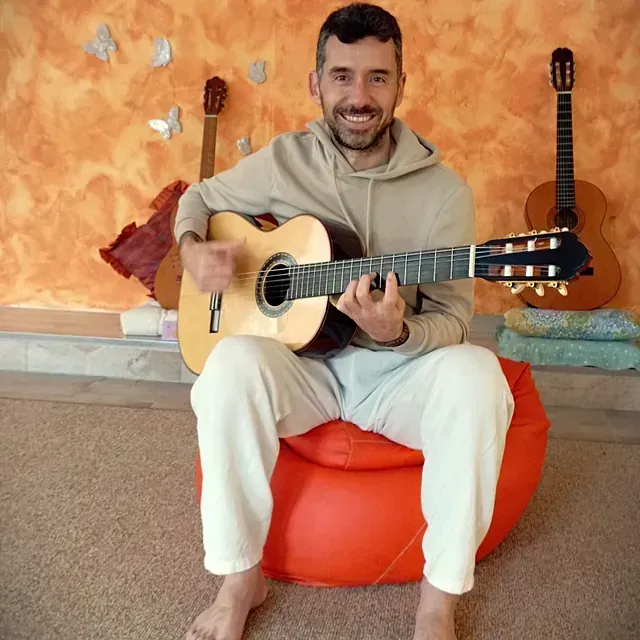 Un hombre está sentado en un sillón puf tocando una guitarra acústica.