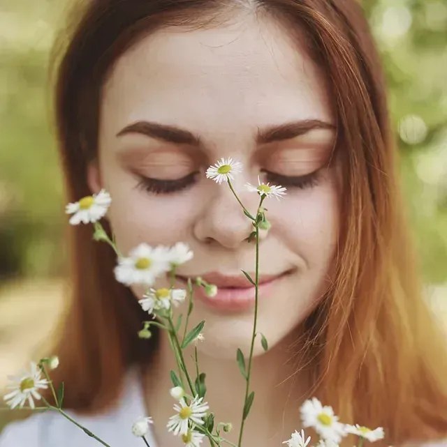 Un primer plano de una mujer oliendo flores con los ojos cerrados.