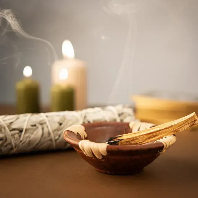 Un cuenco de palo santo junto a una rama de salvia blanca y velas.