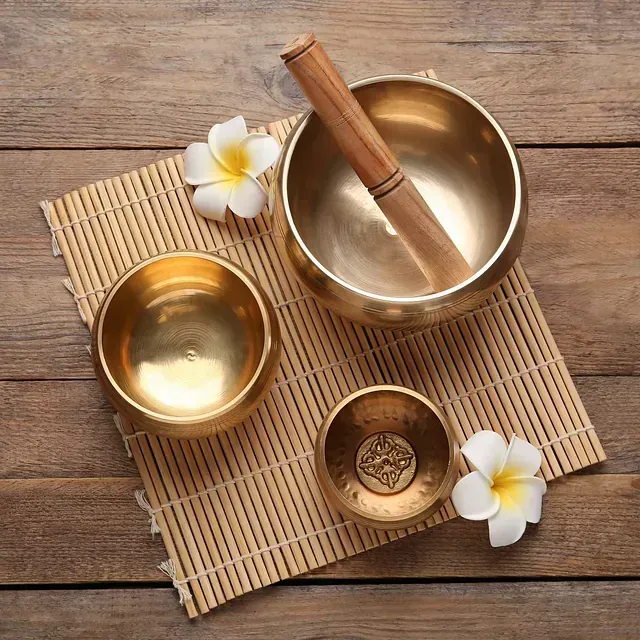 Tres cuencos de latón con asas de madera y flores sobre una estera de bambú sobre una mesa de madera.