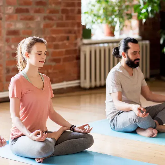 Un grupo de personas está sentada sobre colchonetas de yoga en posición de loto.