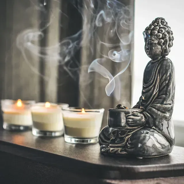 estatua de un niño sosteniendo un porta velas y al lado unos velones de color blanco ensendidos con una esencia de olor 