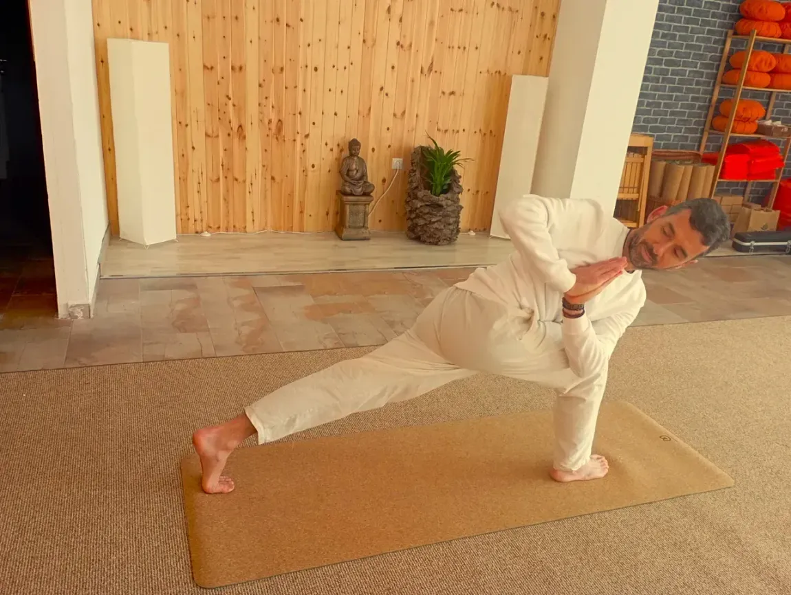 Un hombre con pantalones blancos está haciendo una pose de yoga sobre una colchoneta.
