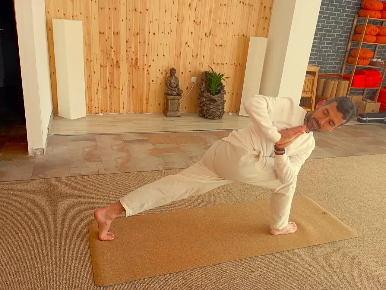 Un hombre con pantalones blancos está haciendo una pose de yoga sobre una colchoneta.