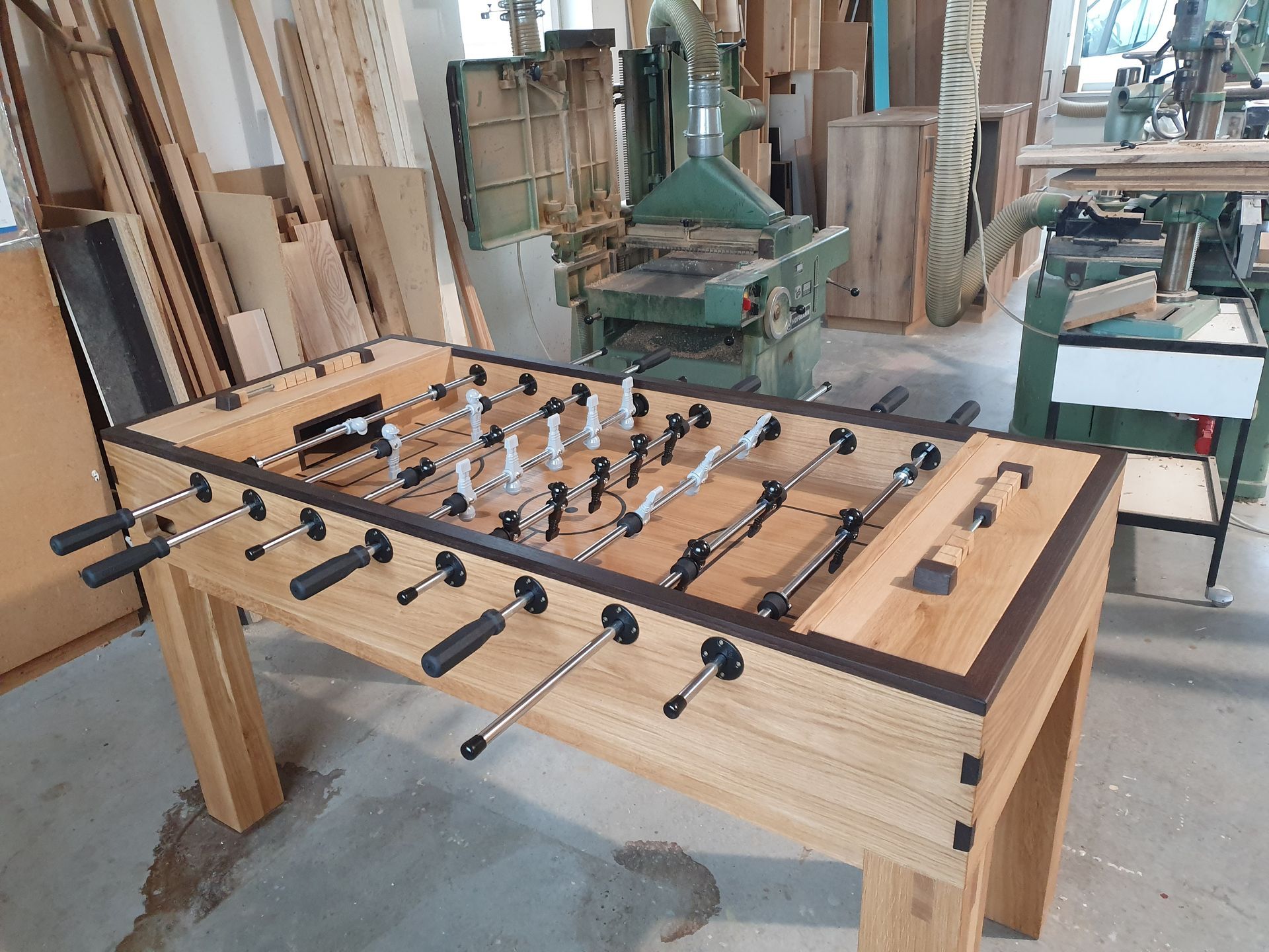 Tischkicker aus hellem Holz in einer Tischlerei, schwarze Griffe und Metallspieler.