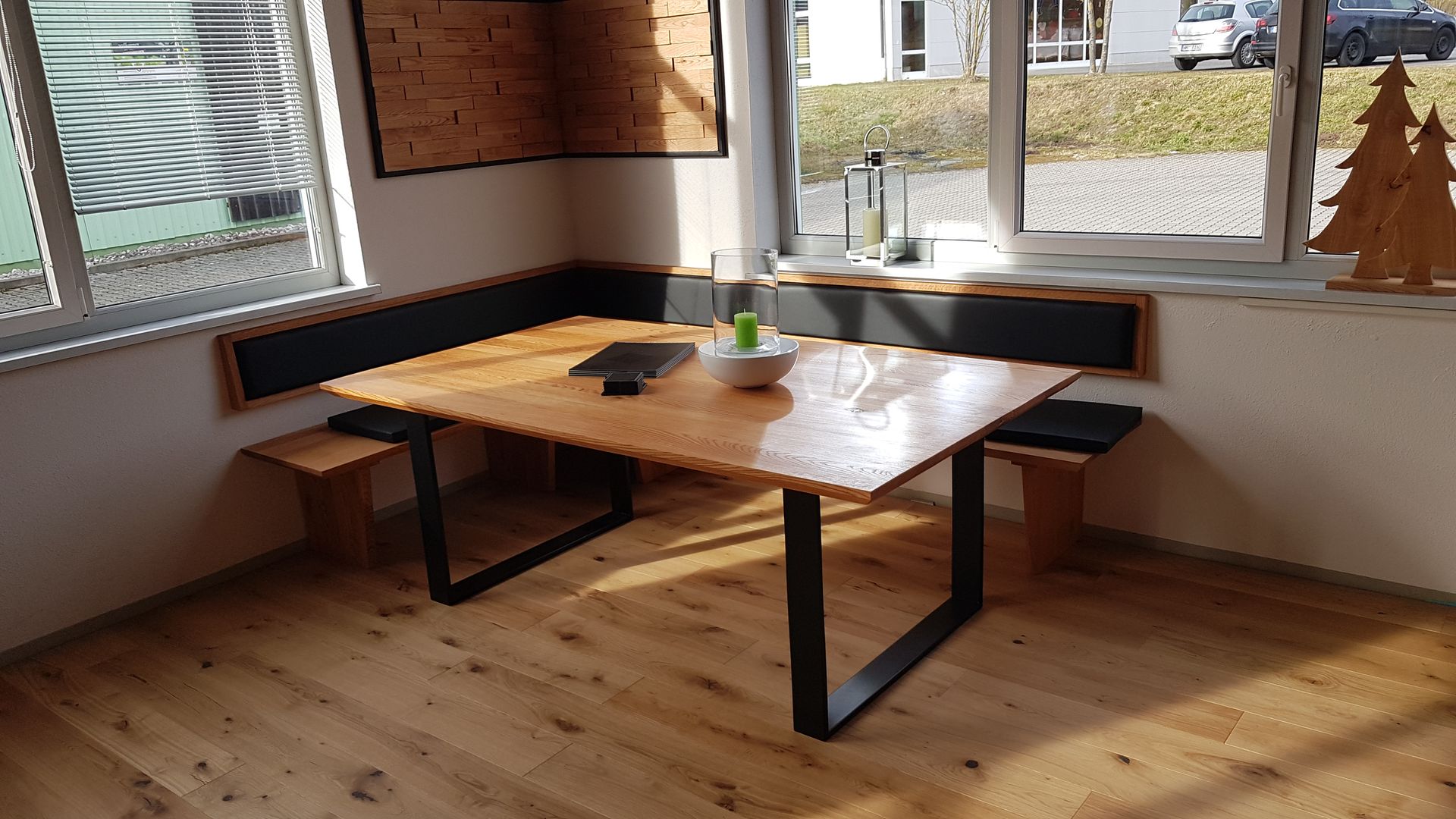 Essgruppe aus Holz in einer sonnigen Ecke: Tisch, Bänke, Ecksitzgruppe und Fenster.