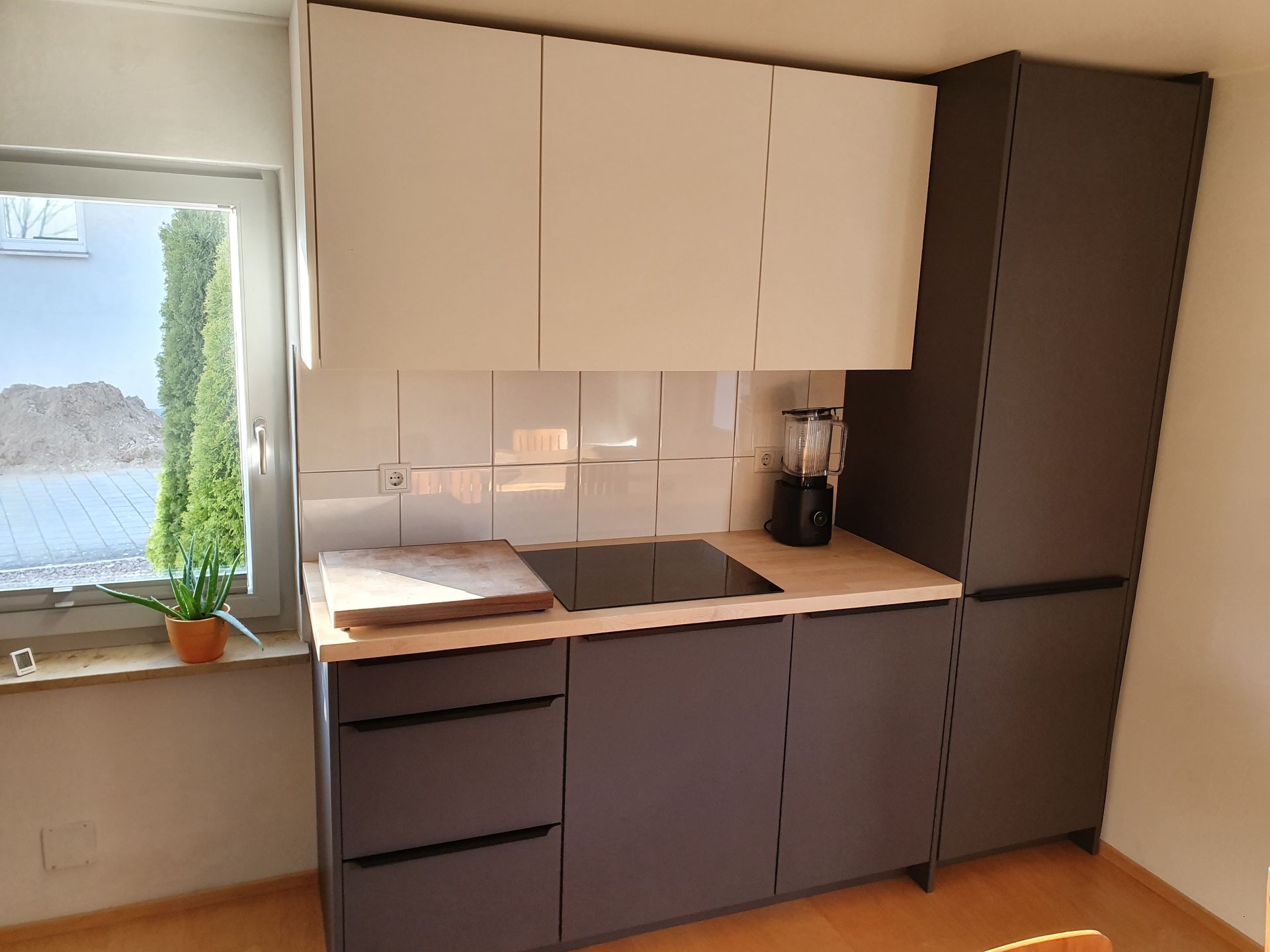 Moderne Küche mit grauen und weißen Schränken, Holzarbeitsplatte und Fenster.